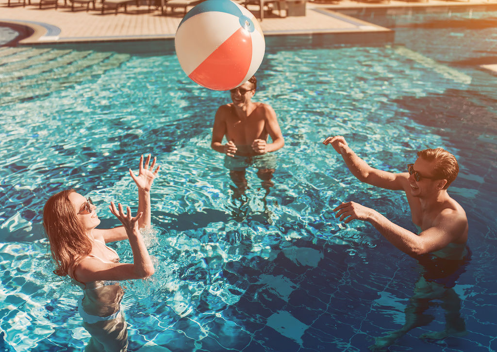 Three friends playing with beachball in pool